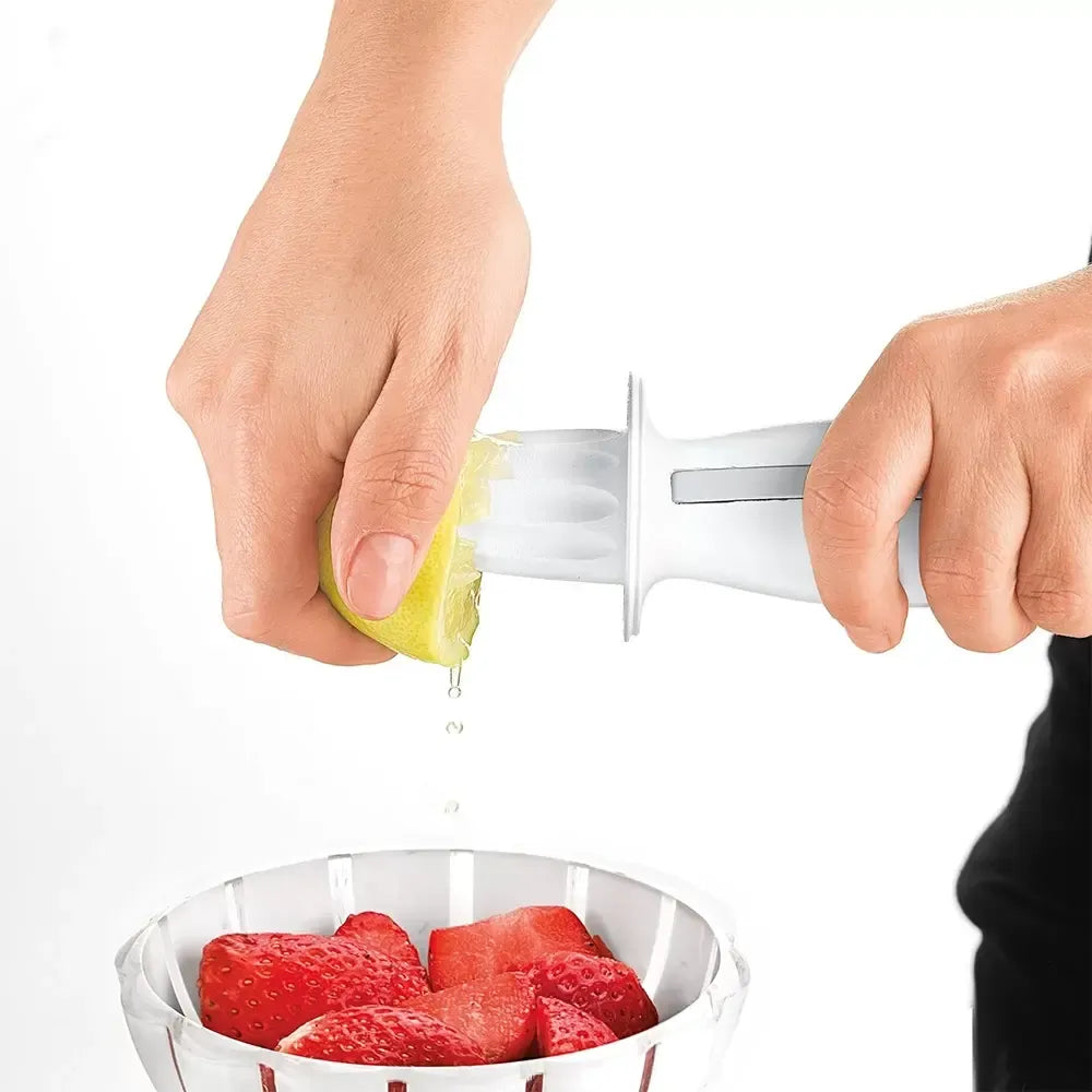Citrusinių vaisių sulčiaspaudė su integruota tarka, balta ir žalia, ant stalo šalia vaisių, pagaminta iš plastiko ir metalo.